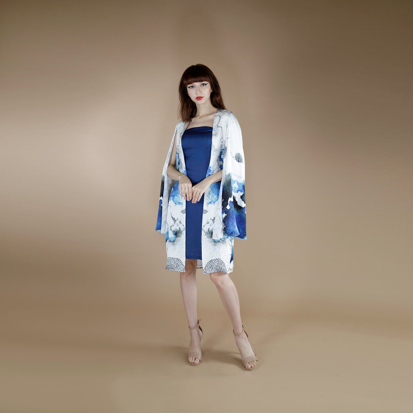Global Small size model wearing a knee length printed cape paired with solid blue tube dress crafted in Organic Lotus Stem fabric, printed and dyed with non toxic GOTS certified inks.
