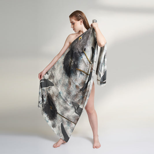 A medium size model draped in an organic rose petal silk fabric scarf, printed with non toxic GOTS certified inks. the scarf has a printed of hazy fields with leaves and flowers flying. 