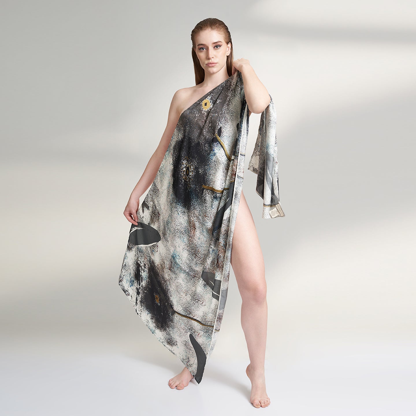 A medium size model draped in an organic rose petal silk fabric scarf, printed with non toxic GOTS certified inks. the scarf has a printed of hazy fields with leaves and flowers flying. 