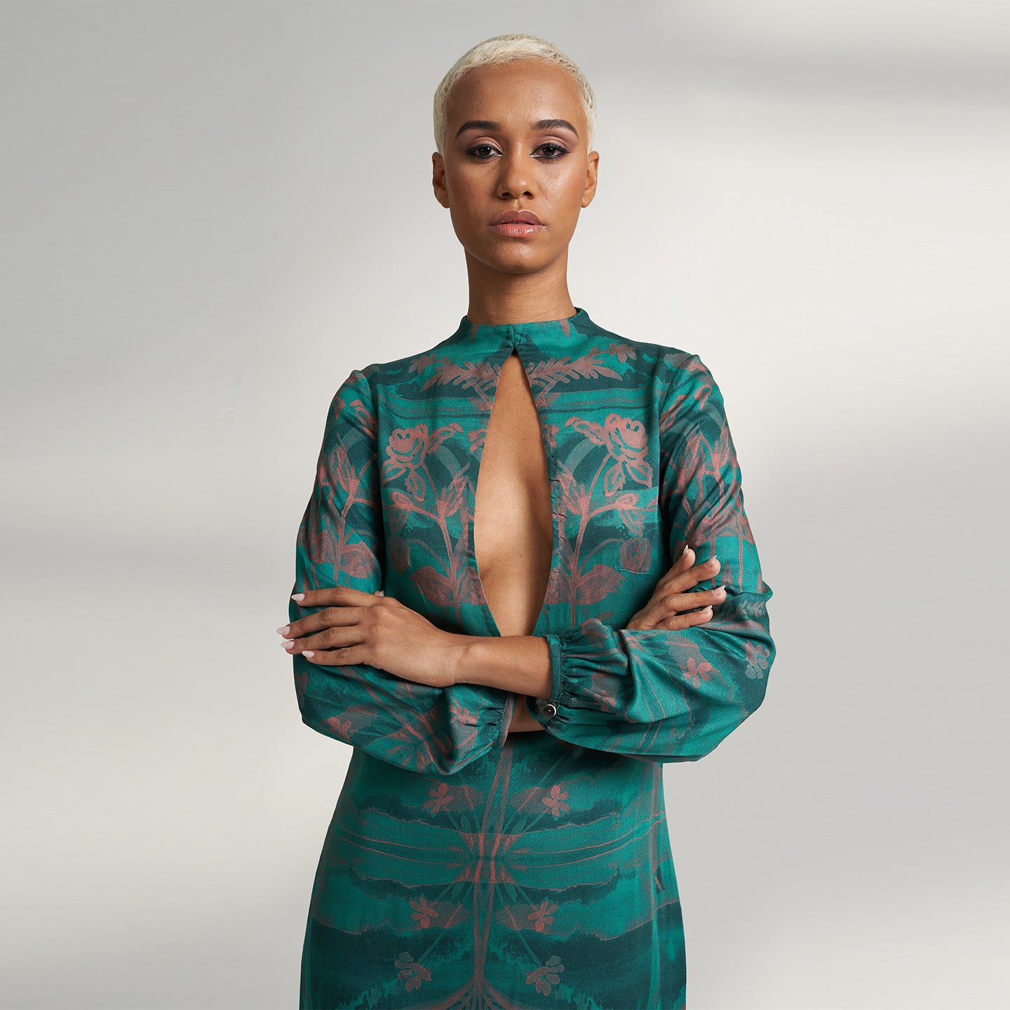 A global small size model wearing a shirt dress printed with hues of green and peach crafted in organic lotus stem silk fabric with a deep front slit neckline and gathered sleeves. the dress is printed with non toxic Gots certified inks. 