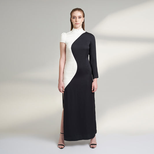A medium size model wearing a black and white half and half dress made from organic lotus stem fabric. This sustainable vegan dress is a long floor length dress with one side pleated in white and one side plain black with a thigh high side slit striking a front pose.