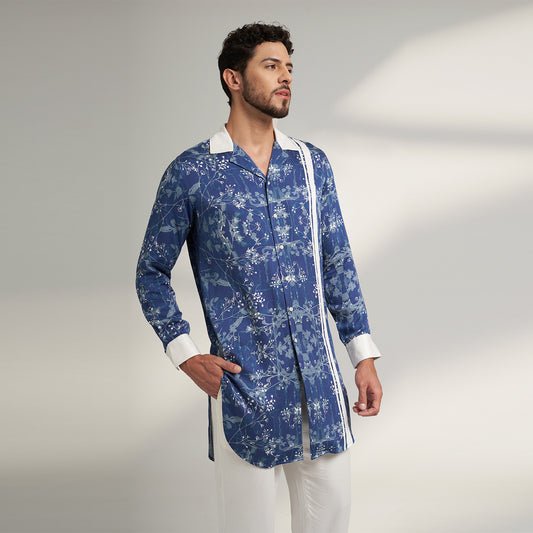 A long cuban collar shirt printed in blue and white made from organic lotus stem fabric white solid cuff and collar in white. the shirt has a comfort fit and it falls at mid thing