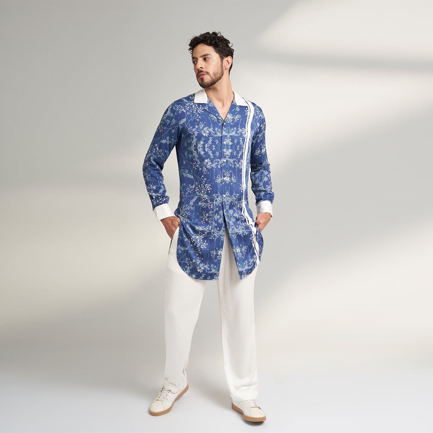 A long Cuban collar shirt printed in blue and white made from organic lotus stem fabric white solid cuff and collar in white. the shirt has a comfort fit and it falls at mid thing