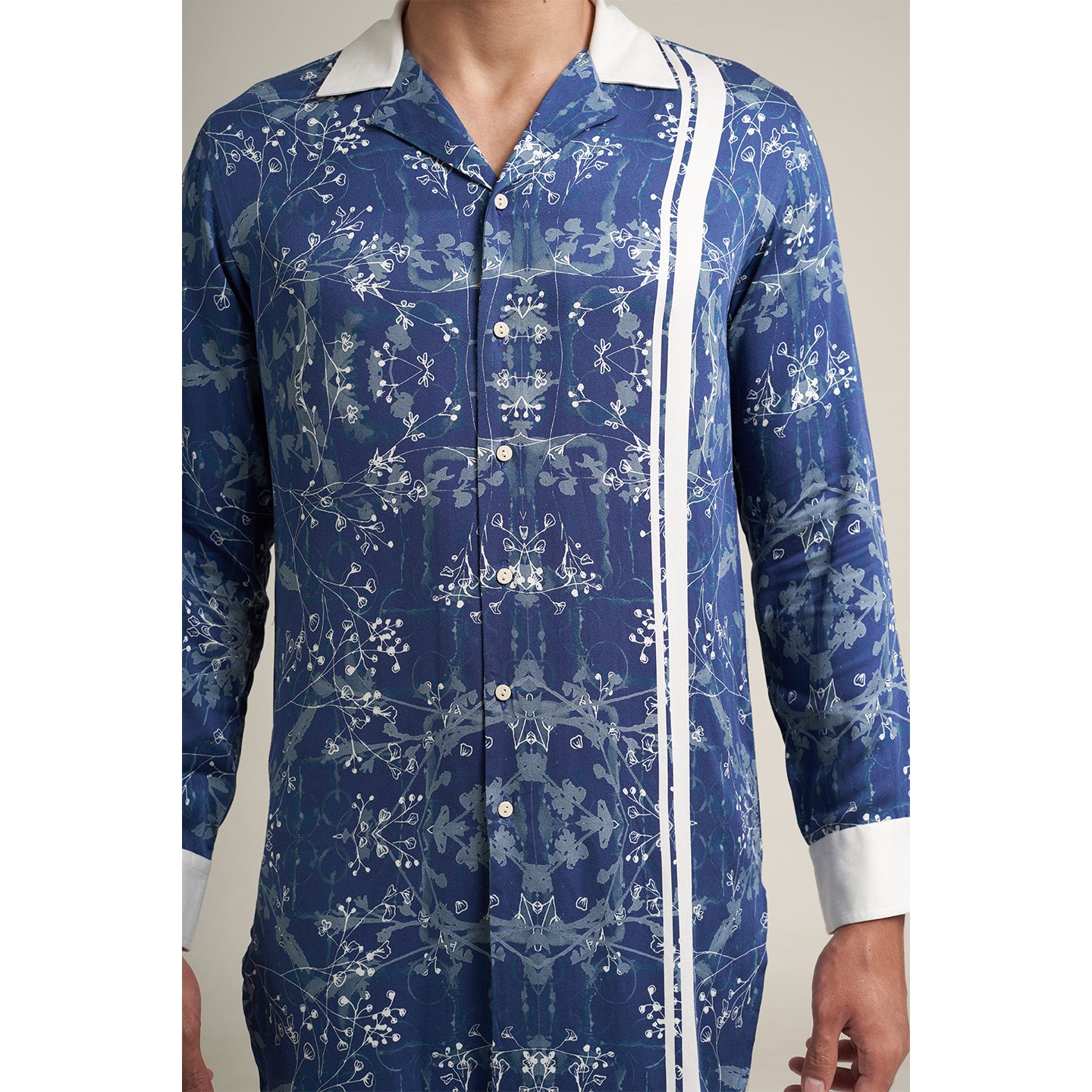 A long cuban collar shirt printed in blue and white made from organic lotus stem fabric white solid cuff and collar in white. the shirt has a comfort fit and it falls at mid thing