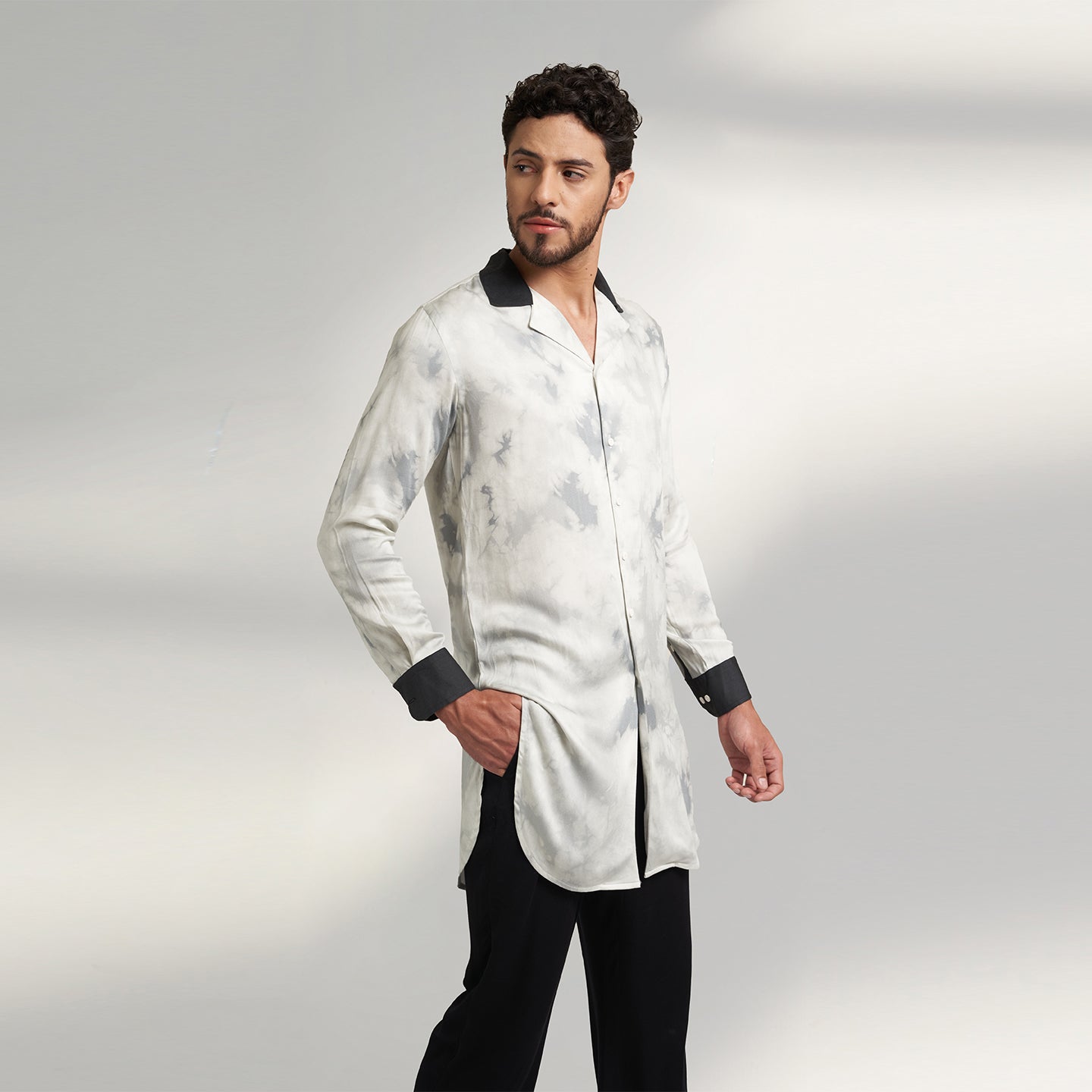 A medium-sized model showcases a Long Printed Cuban Collar shirt in organic Lotus Stem fabric, featuring a solid black collar and cuffs. Paired seamlessly with black trousers made from the same organic lotus stem fabric, presenting a stylish side pose.