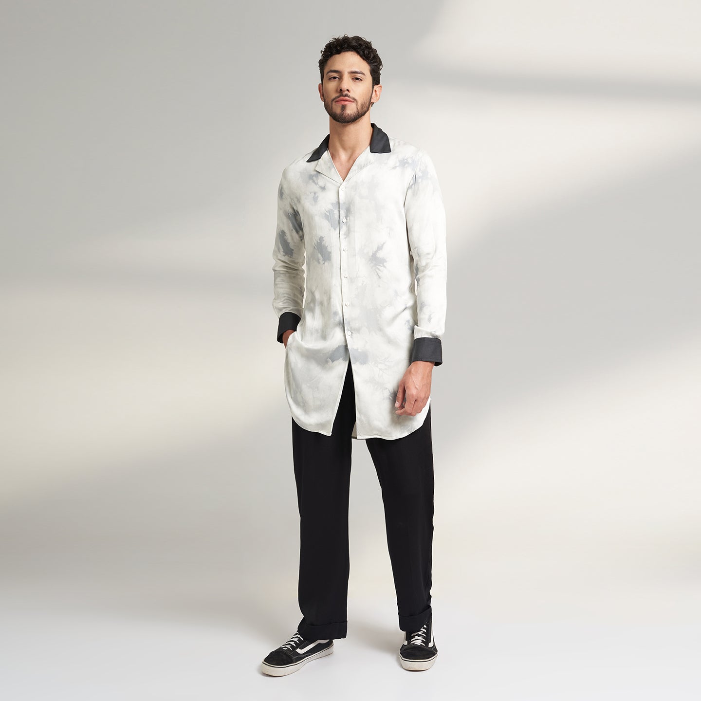 A medium-sized model showcases a Long Printed Cuban Collar shirt in organic Lotus Stem fabric, featuring a solid black collar and cuffs. Paired seamlessly with black trousers made from the same organic lotus stem fabric, presenting a stylish front pose.