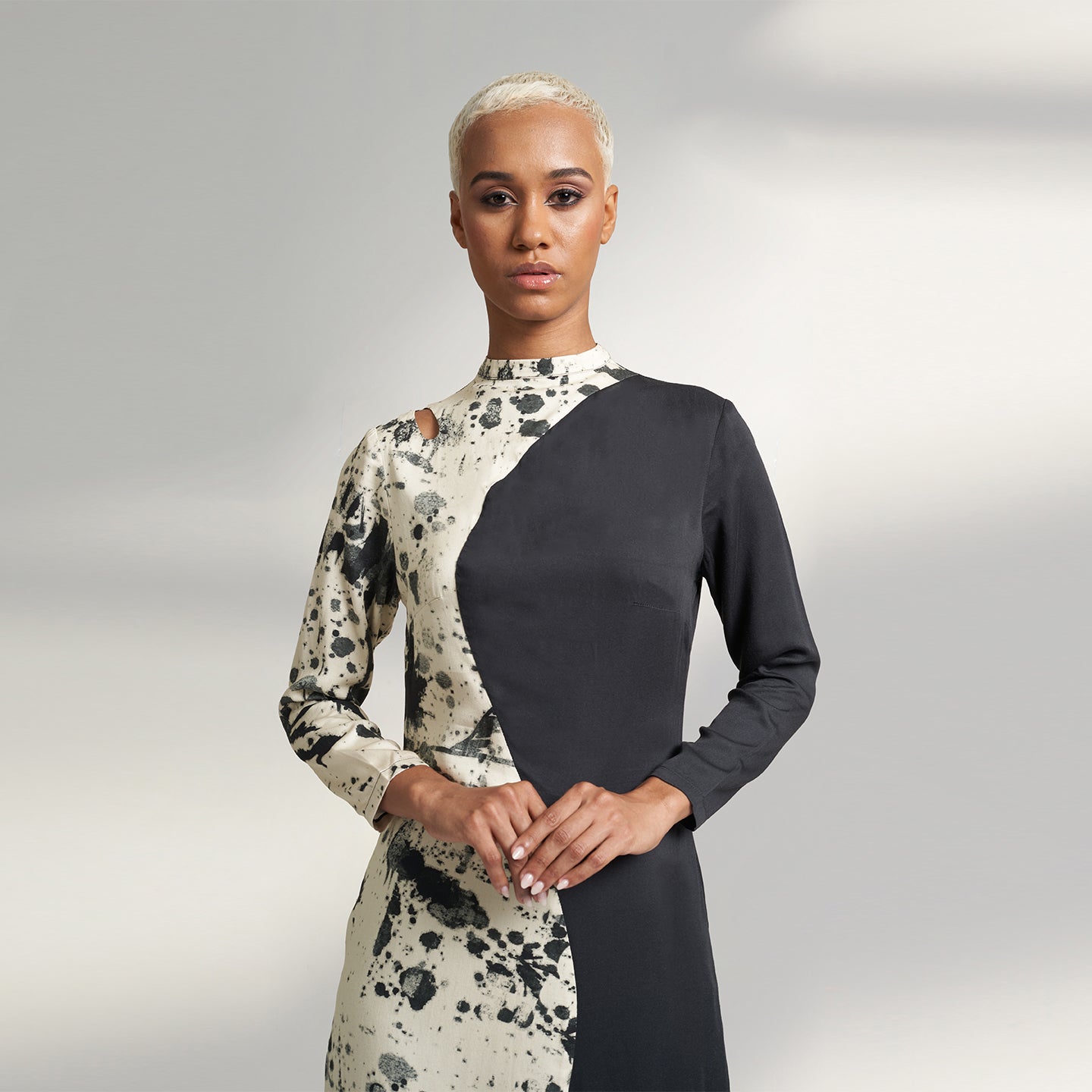 A GLOBAL SMALL SIZE MODEL wearing a black and cream midi dress with one side in solid black and other side in cream with black print on it. the dress is highlighted with a key hole on the right shoulder. 